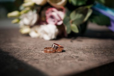 Bir çift alyans, arka planda bir buket çiçek.