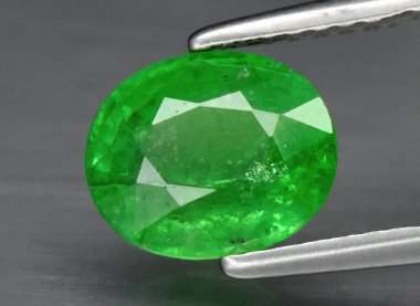 Gri bir arka planda cımbızla doğal yeşil yakut tsavorit. Vanadyum grossular