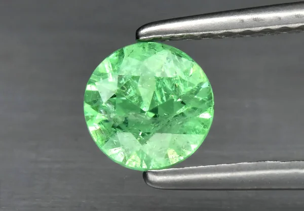 Natural gemstone green garnet tsavorite in tweezers on a gray background. Vanadium grossular — Stock Fotó