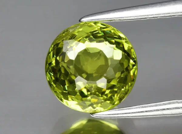 Φυσικό gemstone πράσινο γρανάτη grossular σε τσιμπιδάκι σε γκρι φόντο — Φωτογραφία Αρχείου