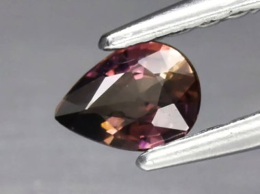 Gri bir arka planda cımbızla doğal değerli taş pembe Safir.