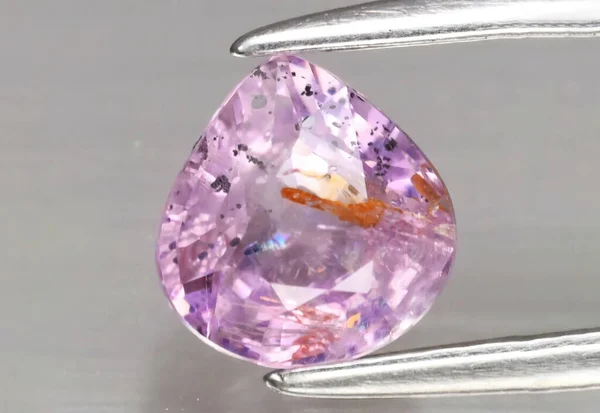 Natural gemstone pink Sapphire in tweezers on a gray background — Fotografia de Stock