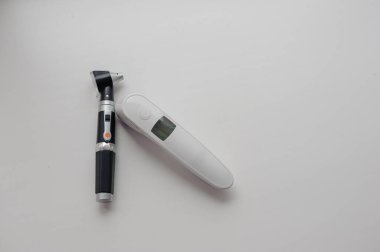 Vücut sıcaklığını ölçmek için beyaz arka planda temas olmayan termometre. Arka planda otoskop, kulak ve orta kulağı incelemek için bir aygıt