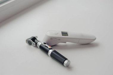 Vücut sıcaklığını ölçmek için beyaz arka planda temas olmayan termometre. Arka planda otoskop, kulak ve orta kulağı incelemek için bir aygıt