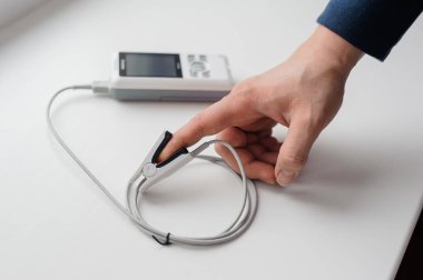 Parmak nabız oksimetresi kullanan bir adam, sağlık izleme konsepti. Arka planda nabız oksimetresi