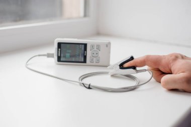 Parmak nabız oksimetresi kullanan bir adam, sağlık izleme konsepti. Arka planda nabız oksimetresi