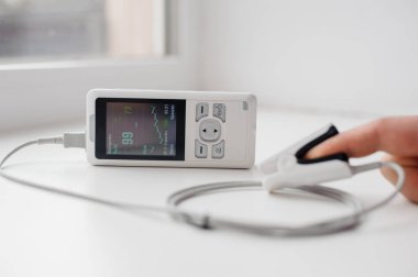 Parmak nabız oksimetresi kullanan bir adam, sağlık izleme konsepti. Arka planda nabız oksimetresi