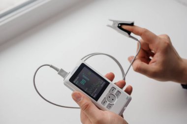 Parmak nabız oksimetresi kullanan bir adam, sağlık izleme konsepti. Arka planda nabız oksimetresi