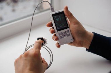 Parmak nabız oksimetresi kullanan bir adam, sağlık izleme konsepti. Arka planda nabız oksimetresi