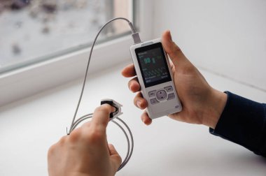 Parmak nabız oksimetresi kullanan bir adam, sağlık izleme konsepti. Arka planda nabız oksimetresi