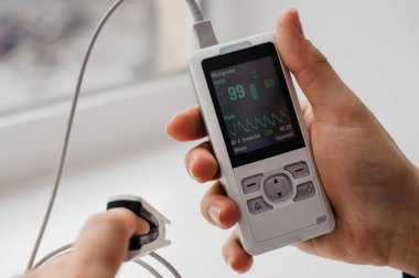 Parmak nabız oksimetresi kullanan bir adam, sağlık izleme konsepti. Arka planda nabız oksimetresi