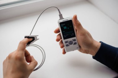 Parmak nabız oksimetresi kullanan bir adam, sağlık izleme konsepti. Arka planda nabız oksimetresi