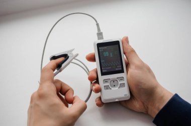 Parmak nabız oksimetresi kullanan bir adam, sağlık izleme konsepti. Arka planda nabız oksimetresi