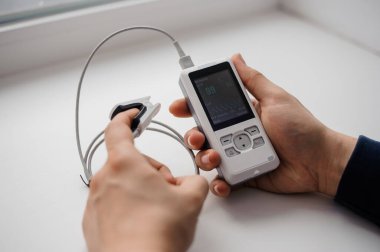 Parmak nabız oksimetresi kullanan bir adam, sağlık izleme konsepti. Arka planda nabız oksimetresi