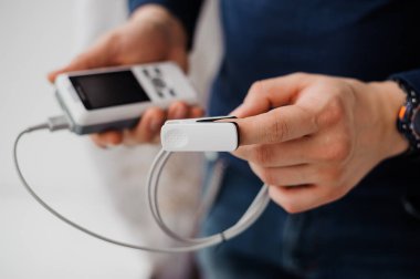 Parmak nabız oksimetresi kullanan bir adam, sağlık izleme konsepti. Arka planda nabız oksimetresi