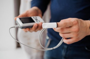 Parmak nabız oksimetresi kullanan bir adam, sağlık izleme konsepti. Arka planda nabız oksimetresi