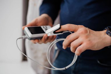 Parmak nabız oksimetresi kullanan bir adam, sağlık izleme konsepti. Arka planda nabız oksimetresi