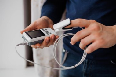 Parmak nabız oksimetresi kullanan bir adam, sağlık izleme konsepti. Arka planda nabız oksimetresi