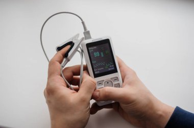 Parmak nabız oksimetresi kullanan bir adam, sağlık izleme konsepti. Arka planda nabız oksimetresi