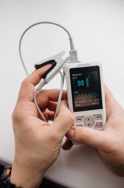 Parmak nabız oksimetresi kullanan bir adam, sağlık izleme konsepti. Arka planda nabız oksimetresi