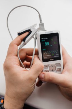 Parmak nabız oksimetresi kullanan bir adam, sağlık izleme konsepti. Arka planda nabız oksimetresi