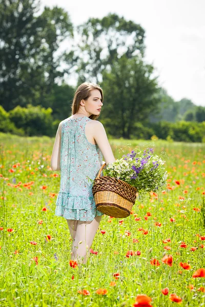 Young woman with a basket full of flowers in a field — Stock Photo, Image