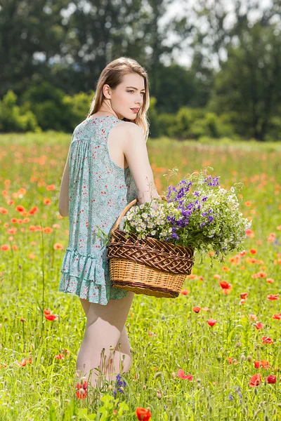 Young woman with a basket full of flowers in a field — Stock Photo, Image