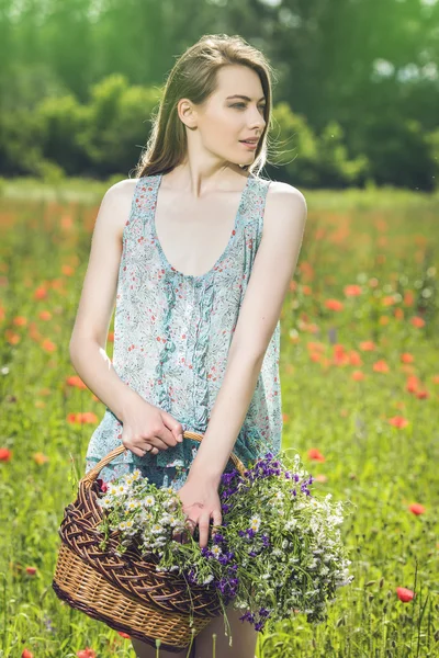 Young woman with a basket full of flowers in a field — Stock Photo, Image