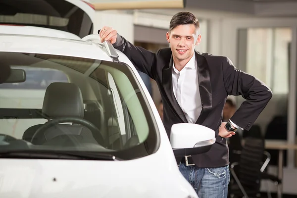 Propietario del coche feliz. Jóvenes guapos apoyándose en su coche nuevo en el concesionario — Foto de Stock