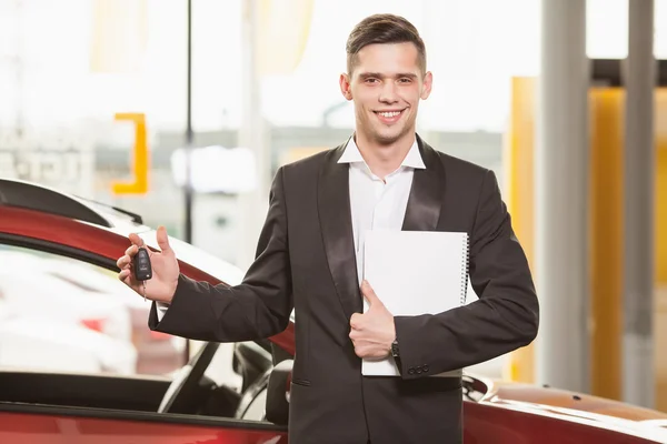 ¡Gran elección! Guapo joven vendedor de coches clásicos de pie en el concesionario con una llave —  Fotos de Stock
