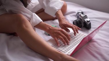 Fotoğrafçı genç bir kadın evinde yatağında otururken defter bilgisayarı kullanıyor..
