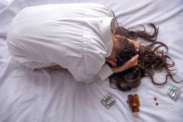 Yatakta depresyondaki genç bir kadın, dağınık saçlı. Çok fazla ilaç alıyor ve anksiyete ve umutsuzluk içinde..