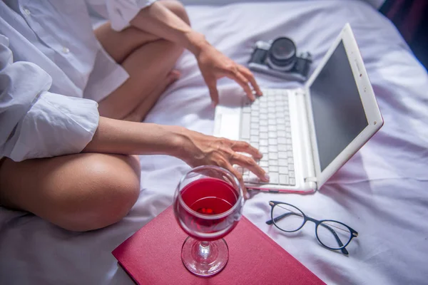 Yatak odasındaki bilgisayarda çalışırken şarap içen iş kadını.