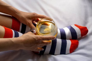 Çizgili çorap giyen ve elinde bir bardak yeşil çay tutan bir kadın.