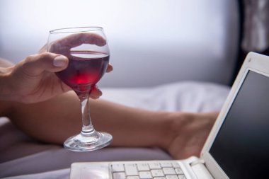 Yatak odasındaki bilgisayarda çalışırken şarap içen iş kadını.