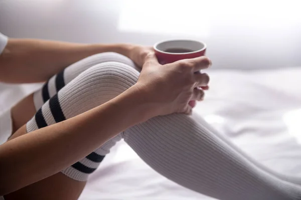 Çizgili çorap giyen ve elinde kahve tutan bir kadın.