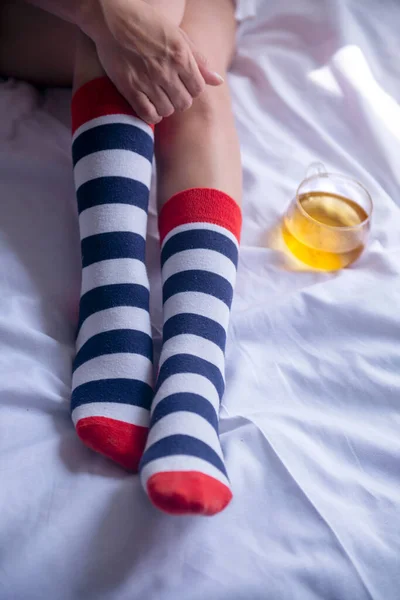 Çizgili çorap giyen ve elinde bir bardak yeşil çay tutan bir kadın.