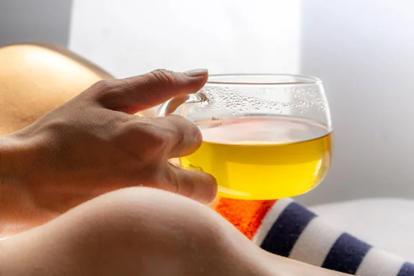 Çizgili çorap giyen ve elinde bir bardak yeşil çay tutan bir kadın.