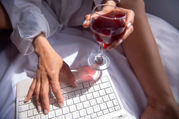 Yatak odasındaki bilgisayarda çalışırken şarap içen iş kadını.