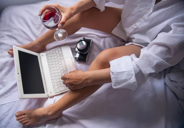 Yatak odasındaki bilgisayarda çalışırken şarap içen iş kadını.