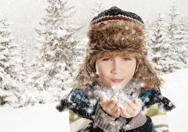 Felice ragazzo soffiando fiocchi di neve nel paesaggio invernale — Foto Stock