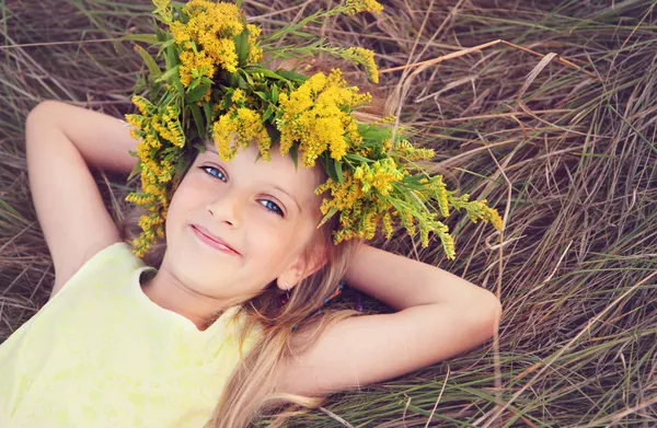 Glad liten flicka i blommor krona på gräset — Stockfoto