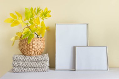 İki gümüş çerçeve dikey A4 ve yatay A5 şablonu, sıcak sonbahar atkısı örgü ve ahşap sepetteki sonbahar sarı yaprakları..