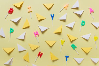 Sarı arkaplan üzerinde farklı harflerle birçok renkli kağıt üçgen ve doğum günü mumları olan soyut bir arkaplan.