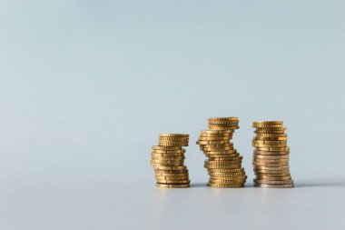 Three stacks of yellow coins on blue background. Image with copy blank space.