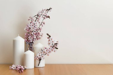 Beyaz mumlar ve ahşap masanın üzerinde pembe bahar sakura çiçekleri olan basit bir kompozisyon. Boş alanı kopyalayan resim.