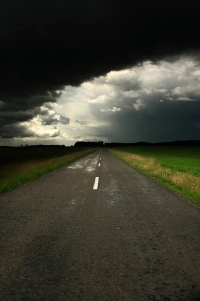 Droga asfaltowa i ciemne chmury nad nim — Zdjęcie stockowe