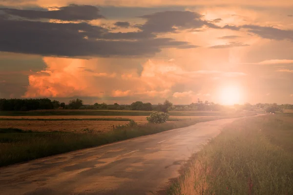 Route asphaltée avec nuages et rayon de soleil au coucher du soleil — Photo