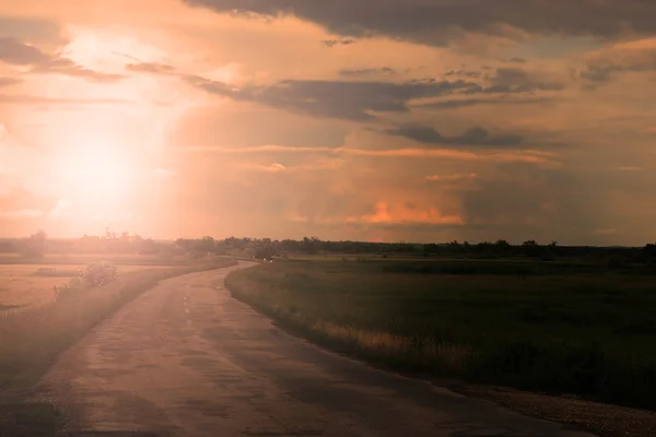 Strada asfaltata con nuvole e raggio di sole al tramonto — Foto Stock