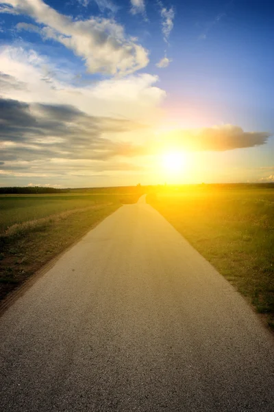 Estrada de asfalto com nuvens e raios de sol ao pôr do sol — Fotografia de Stock